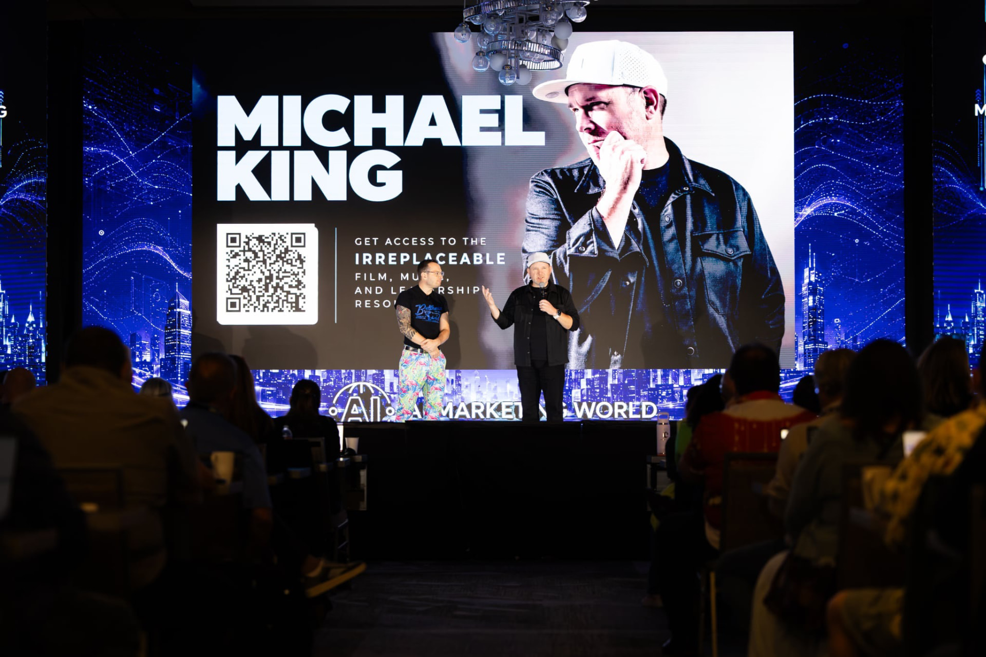 Michael King Jr. speaking on the AI Marketing World stage in Dallas beside Austin Armstrong, with the IRREPLACEABLE screen behind them